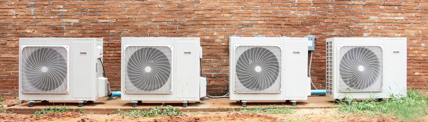 Front view of a row of air conditioning compressors in front of a brick wall